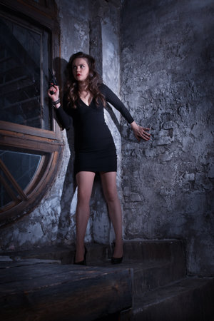Noir film style woman in a black suit posing with a gunの写真素材