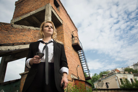 Noir film style woman in a black suit posing with a gunの写真素材