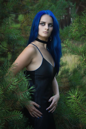 Beautiful woman with dark blue hair dressed in black dress in the magic forest. Gothic style. 