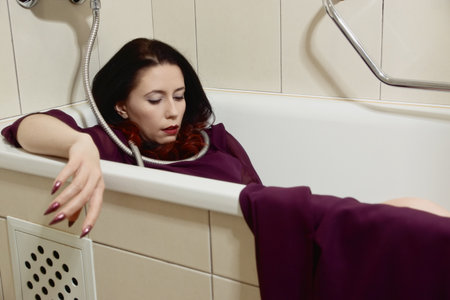 Lifeless beautiful woman lies in a bathtub. She is strangled with a shower hose