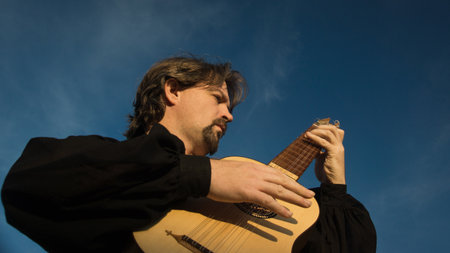 Adult man in historical suit playing vihuela in summer garden