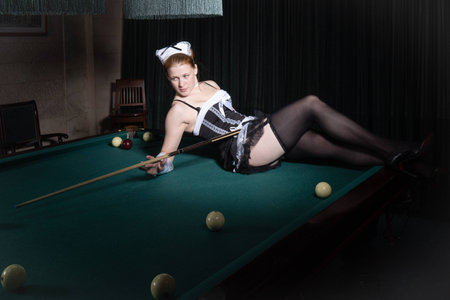 Young sexy chambermaid plays billiard. Pin up style.
