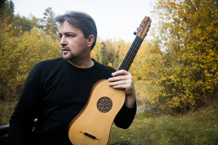 Adult man playing renaissance guitar in autumn gardenの写真素材