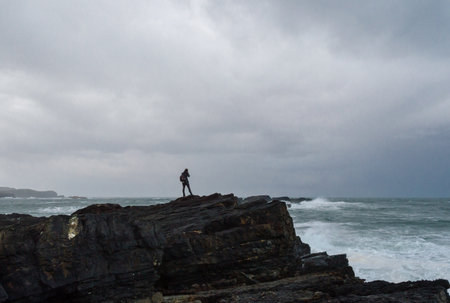 woman photographing on the edge of a cliff before a storm in the Cantabrian sea.の写真素材