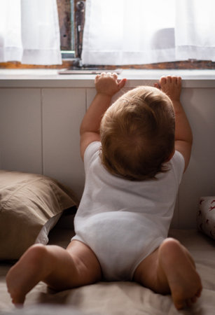 Happy baby sitting on bed playing and looking in window at home