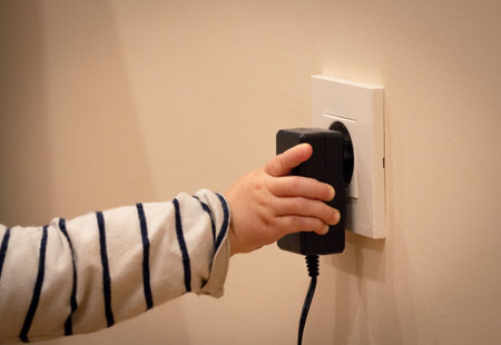 Little child's hand playing with power socket and electric transformer. Closeup.