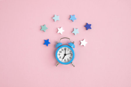 Blue alarm clock on a pink background, decorated with white, blue and green stars around. Bedtime concept, Christmas composition, insomnia, reminder, starfall, romantic date.place for logo. Copyspaceの写真素材