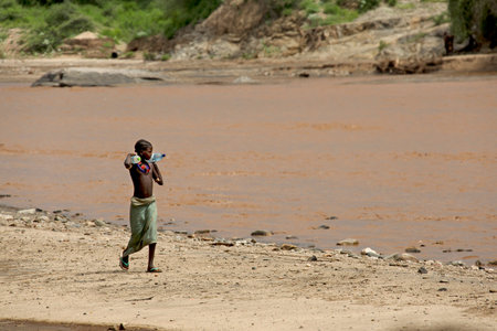 SOUTH OMO - ETHIOPIA - November 24, 2011: Unidentified african girl goes on the river bank and bears bottles with water on November 24, 2014 in South Omo, Ethiopia.のeditorial素材