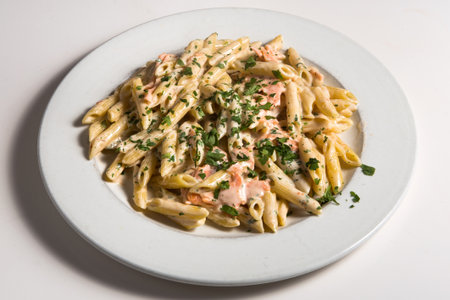 Fish Penne Pasta Al Dente with Salmon, Red Caviar, Parmigiano Reggiano Cheese, Spices and Basil in Restaurant Plate Isolated on White Background Close Up. Traditional Italian Macaroniの写真素材