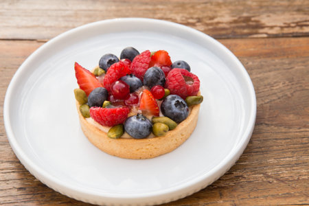 Tasty tartlet with berries on a white plate. Wooden background.の写真素材