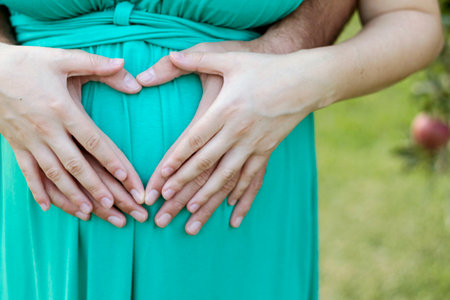 Fingers of a couple forming heart shape on pregnant woman belly