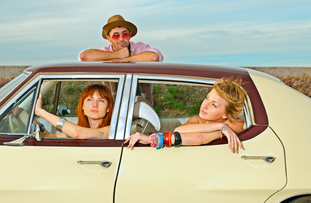 Two young girls and a guy posing in an old American car parked at the curb 