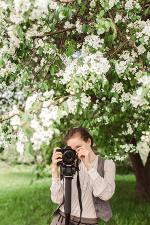 Woman shoots at the camera on a tripod, monopod against a background of trees, park, apple blossom