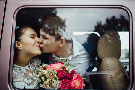 The groom kisses the bride, the view through the glass of the carの写真素材