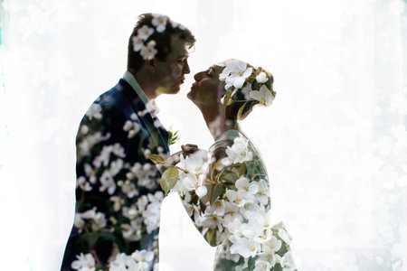 Happy newlyweds kissing. Brunette bride  and  groom stand  silhouettes of happy double exposure, multiple exposure apple blossomsの写真素材