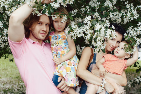 Family: mother, father and two daughters under a flowering apple tree in bright clothes in the parkの写真素材