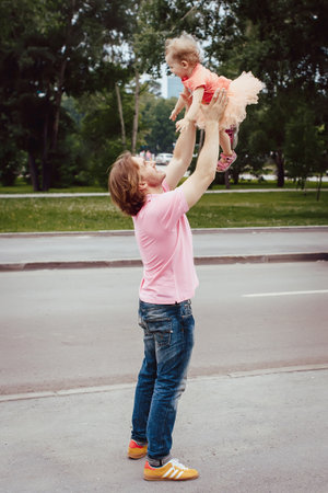 Dad in the park playing with her baby by throwing daughter up, Dad and daughter dressed in the pink, Dad and daughter happy family laughingの写真素材
