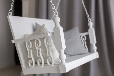 White swing with pillow with beautiful wooden handles with carved wood