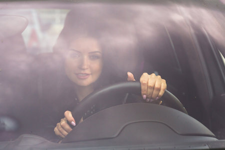 Woman holding hands on steering wheel front viewの写真素材