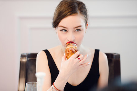 Woman biting in a croissant in a cafe interiorの写真素材