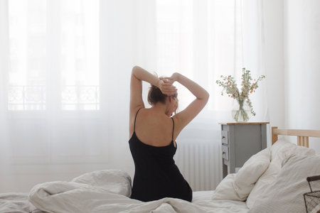 Back view of woman sitting on bed in the morningの写真素材