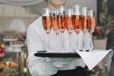 Faceless man in uniform holding tray with filled champagne glasses while serving on event.の写真素材