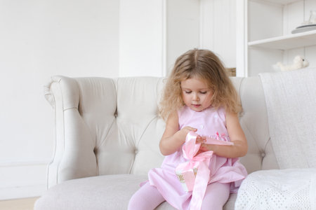 Adorable little toddler girl sitting on sofa with pink ribbon.の写真素材