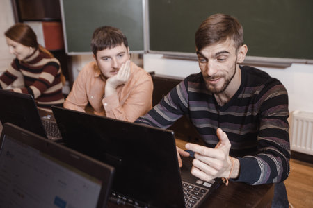 Young man watching laptop with astonishment while studying in class with other students.の写真素材