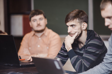 Young man watching laptop with astonishment while studying in class with other students.