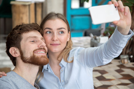Content man and woman posing for selfie using smarpthone.の写真素材