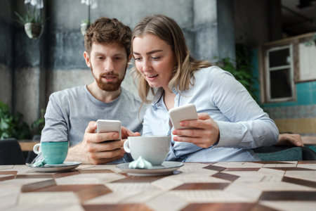 Young couple interacting while using smartphones and drinking coffee in shop.の写真素材