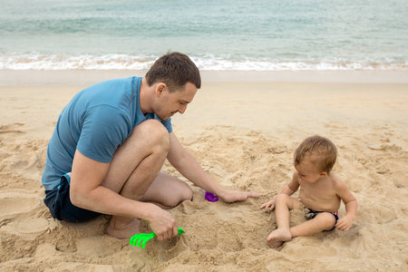 Young father with baby spending time on sandy beach playing while having vacation.の写真素材