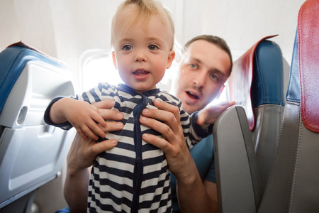 Father and baby son during flight on airplane going on vacations. Dad holding baby boy on a chair. Air travel with baby, child and family concept.の写真素材