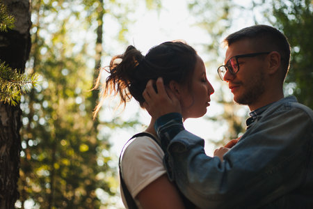 A beautiful young couple kiss and hug in a summer park near treesの写真素材