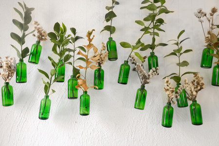 Wall with hanging green bottles and stick in flowers and green branches.の写真素材