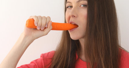 Smiling woman bites carrot. Isolated studio portrait. Long hair girl.の写真素材