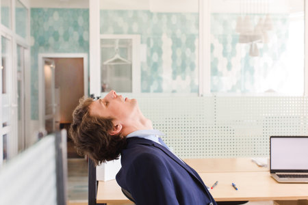 Side view of man leaning back in chair with eyes closed and masturbating at work dreaming of erotic scenesの写真素材