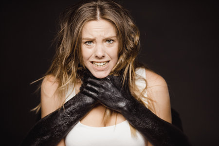 Concept photo of young frightened girl being chocked by terrifying black hands from behind on black backgroundの写真素材