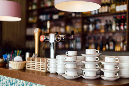 Stacked and prepared ceramic cups with saucers placed on wooden counter of a barの写真素材
