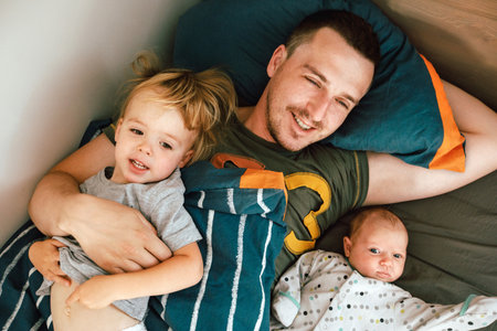 From above view of young handsome man in T-shirt sleeping in bed under blanket with little girl and...