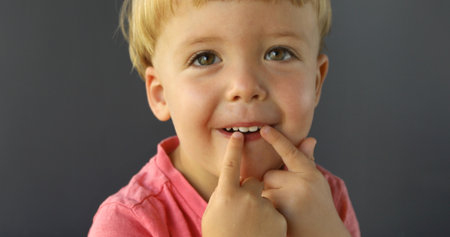 Pretty boy on a gray background. He points his fingers of both hands on his teeth and smile. Dentist...