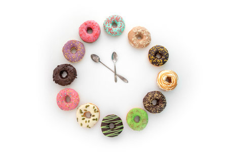 From above clock made of variety tasty doughnuts and spoons isolated on white background as sign of sweet breakの写真素材