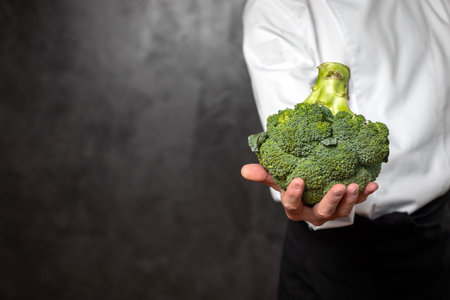 The hand of a young man is holding a floret of broccoliの写真素材