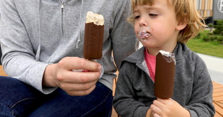 Dad and son eating ice cream on bench in the park on dayの写真素材