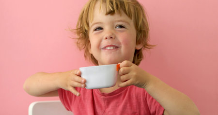Happy child drinks milk from a cup on pink backgroundの写真素材
