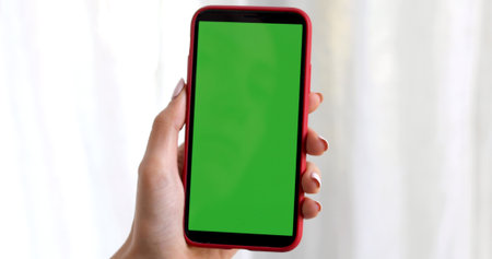 Female hand with a smartphone with a green screen on a white background curtainsの写真素材