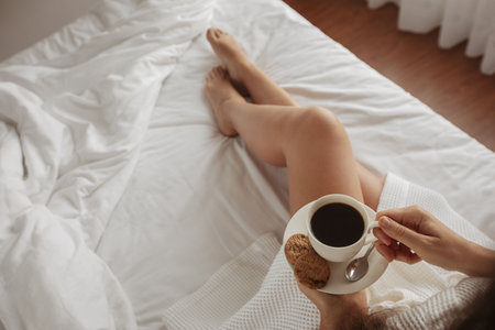 Coffee mug with saucer and cookies background beautiful legs girl who lies bedの写真素材