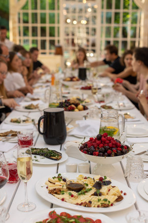 Group of people gathered at long wooden table in restaurant served for party with glasses and...