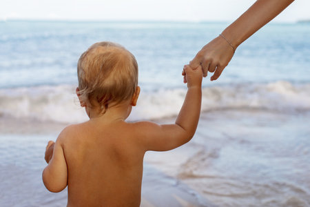 Back view of little child holding hands with crop mother going to water relaxing in seaの写真素材