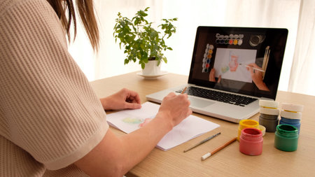 Woman learning to draw on an online course online sitting at home looking over her shoulder. Drawing...
